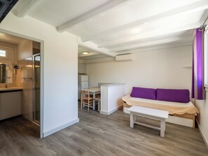 Un espace de vie compact comprenant un coin cuisine, un coin repas et un espace nuit avec un lit et un banc.