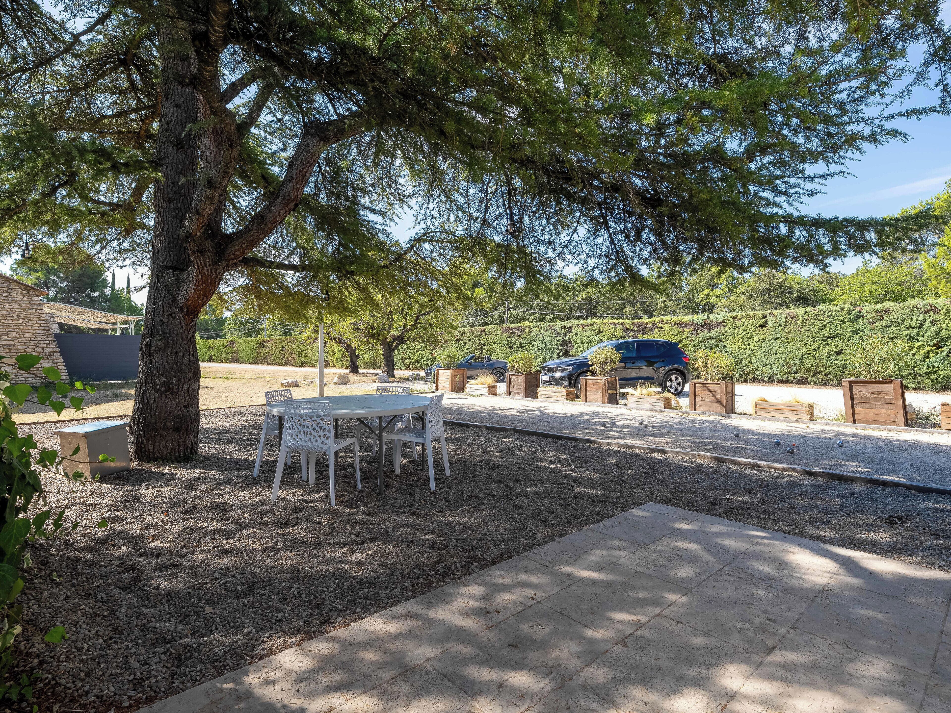 Un patio sterrato con tavolo e sedie, un albero e auto parcheggiate.