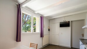 Une pièce comprenant une table à manger, des chaises, un téléviseur fixé au mur, une porte blanche et une fenêtre avec des rideaux.