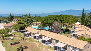 A resort with multiple stone-roofed cottages, a swimming pool, and a view of distant mountains.