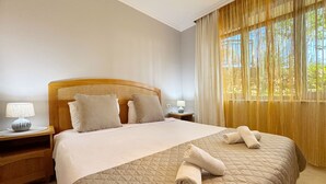 A neatly made bed with a quilted cover, two bedside tables with lamps, and a window with sheer curtains. - Stunning 2-bed Apartment in Sozopol (Sozopol)