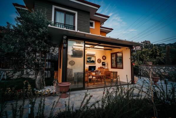 Una casa moderna con un ventanal de vidrio que da a una sala de estar, una pared de piedra y un jardín con plantas en macetas.