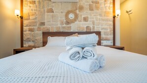 Una cama bien hecha con toallas enrolladas, una pared de piedra y dos lámparas fijadas a la pared.