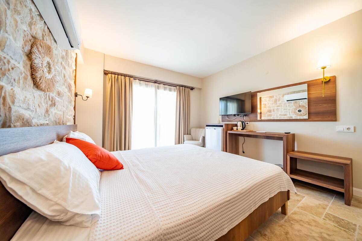 Una habitación de hotel con una cama grande, cabecera de madera, televisor de pantalla plana, escritorio pequeño y pared de acento de piedra.