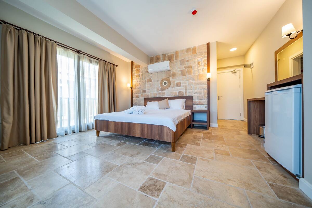 Habitación de hotel con una cama grande, paredes de piedra, un escritorio empotrado y un refrigerador.