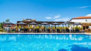 Una piscina azul cristalina con sillas de descanso y sombrillas, rodeada de edificios y árboles.