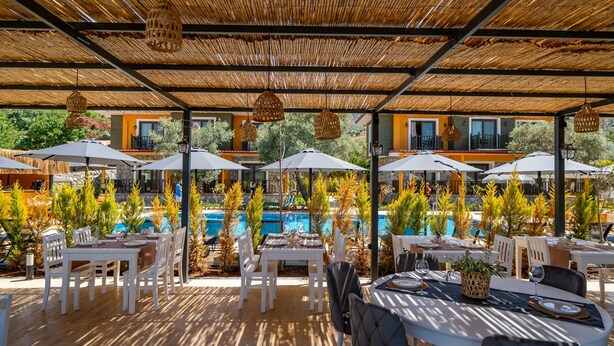 Un área de comedor al aire libre con mesas y sillas, sombrillas y una piscina al fondo.