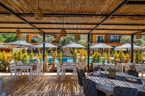 An outdoor dining area with tables and chairs, umbrellas, and a pool in the background. - Selimiye Thales Otel (Marmaris)