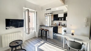 Una cocina moderna con microondas integrado, fregadero y una pequeña zona de bar. Hay dos taburetes y una mesa con una lámpara.