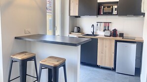 Una cocina moderna con una isla central, taburetes de bar, microondas integrado y un refrigerador compacto.
