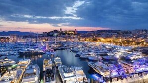 Un puerto deportivo lleno de barcos al atardecer, con edificios y una colina en el fondo.