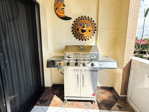 Un barbecue à gaz Char-Broil doté de quatre brûleurs et d’un brûleur latéral, installé sur une terrasse carrelée, avec une porte et un masque décoratif fixé au mur.