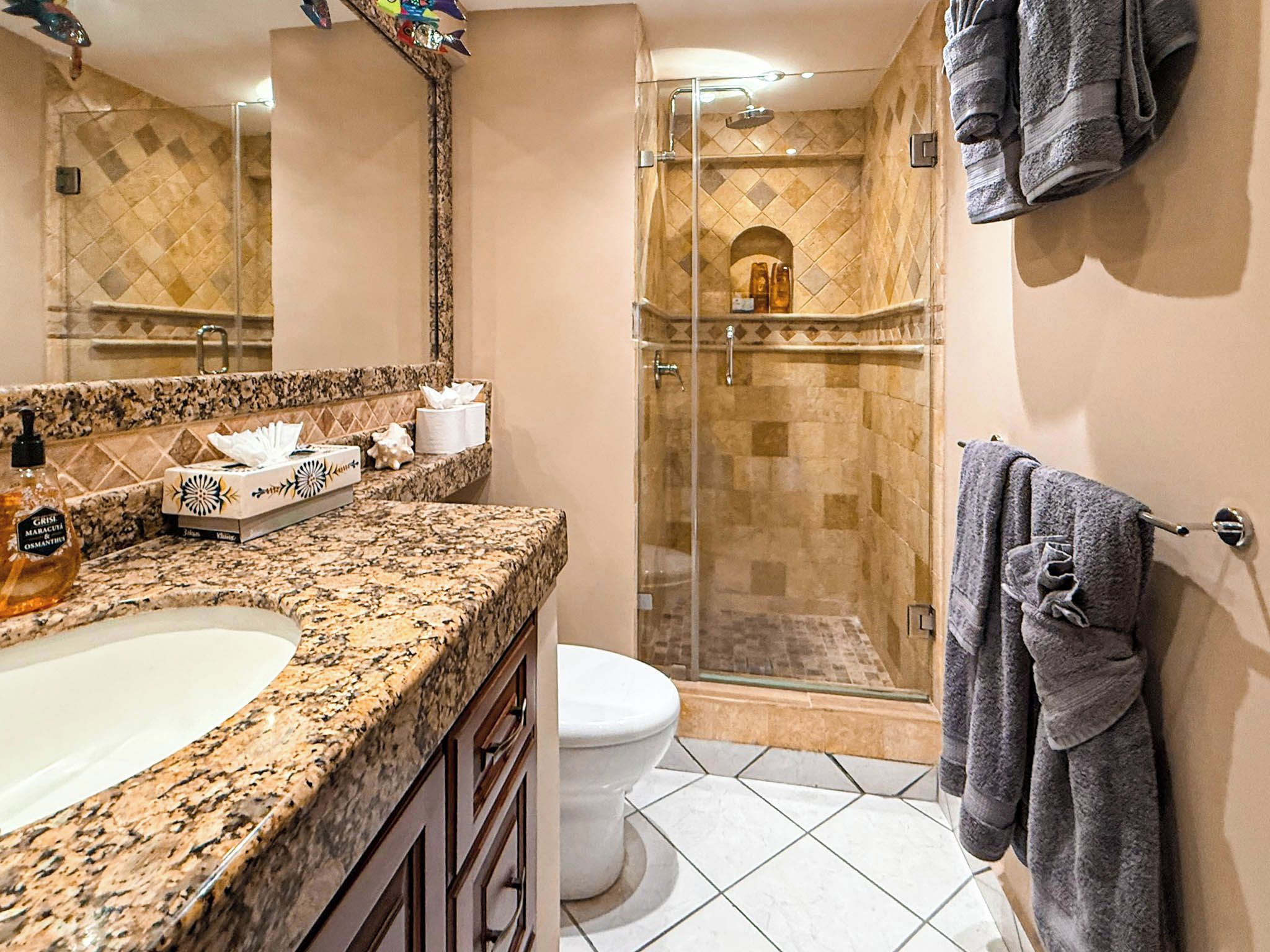 A bathroom with a granite countertop, a white toilet, a glass-enclosed shower, and a towel rack.