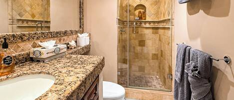 A bathroom with a granite countertop, a white toilet, a glass-enclosed shower, and a towel rack.