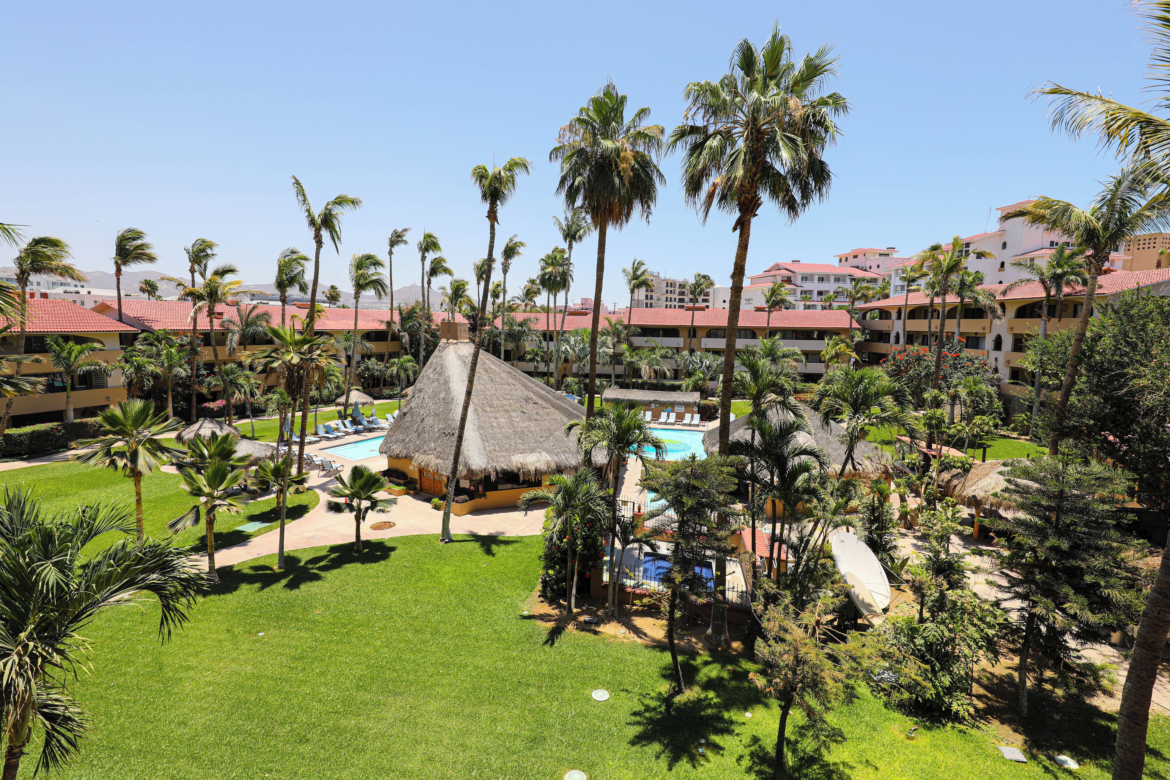 A resort with a pool area, palm trees, and a thatched-roof structure.
