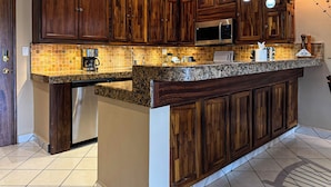 A kitchen with dark wooden cabinets, a granite countertop, a built-in microwave, and pendant lighting. - A-303 Enjoy Your Vacation In This Delightful Remodeled Condominium! (Cabo San Lucas)