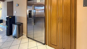 A kitchen with a stainless steel refrigerator, a trash bin, and wooden cabinets. - A-303 Enjoy Your Vacation In This Delightful Remodeled Condominium! (Cabo San Lucas)