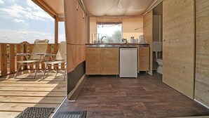 A compact kitchen with wooden cabinets, a sink, and a refrigerator. There is a small window above the sink and a door leading to a bathroom. - Barricata Holiday Village Lodge Tent Deluxe für 5 Personen (Porto)
