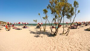 A beach with red and white umbrellas, sun loungers, and people relaxing. - Barricata Holiday Village Lodge Tent Deluxe für 5 Personen (Porto)