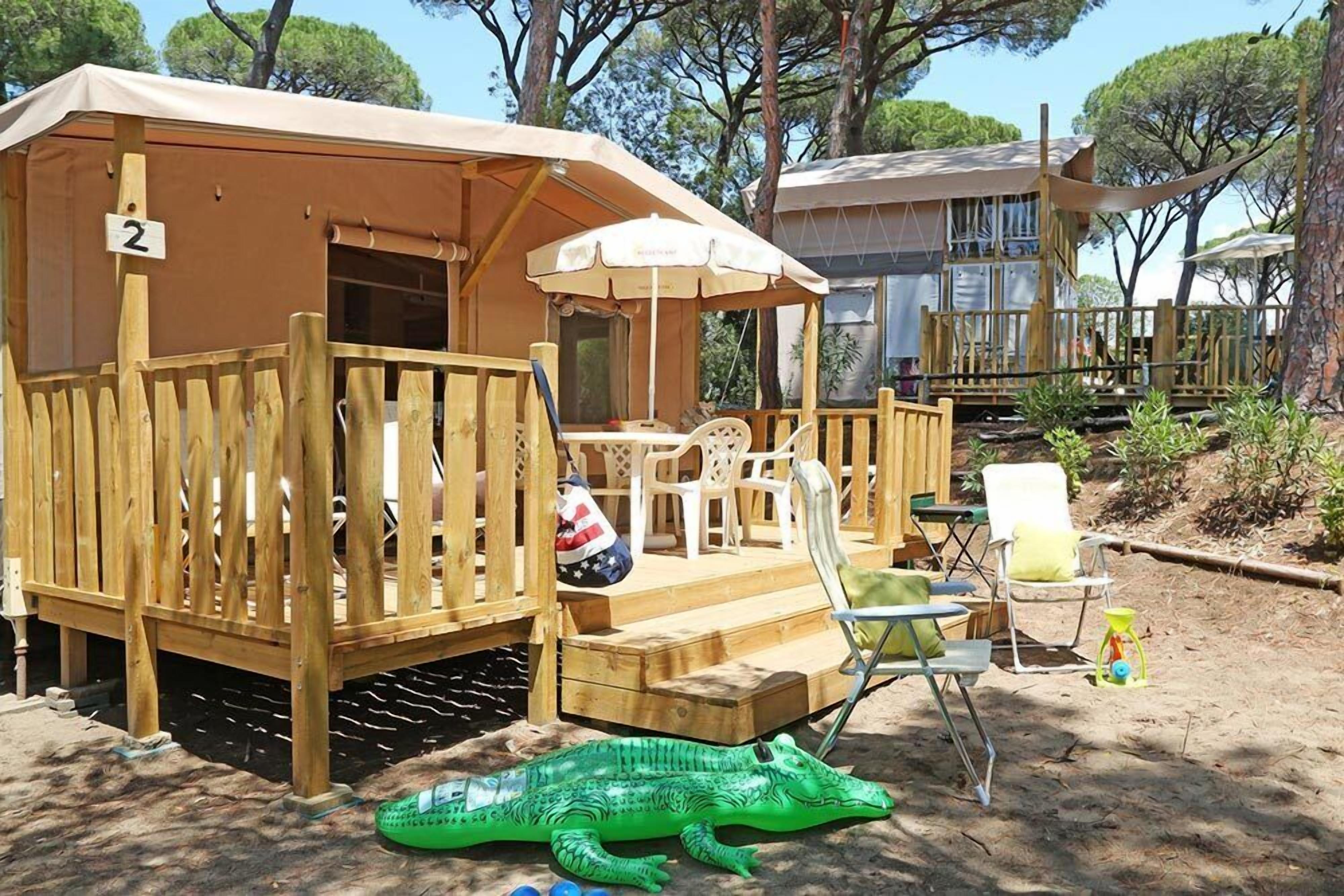 Une terrasse en bois avec un espace salon couvert, un panneau portant le chiffre « 2 » et un crocodile gonflable vert.