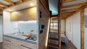 Cocina pequeña con lavamanos, encimera y armarios de madera. Una escalera conduce a una zona de descanso en la mezanina.