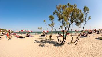 Una spiaggia con ombrelloni rossi e bianchi, lettini e persone che si rilassano.