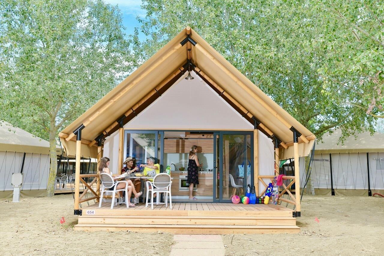 Una struttura in legno con ingresso in vetro, circondata da alberi e terreno sabbioso.