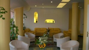 A lobby with a sofa set, armchairs, a glass coffee table with flowers, and a patterned carpet. - Hotel Robinia (Imperia)