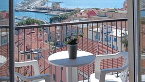 A balcony with a view of a marina, a small table with a potted plant, and white plastic chairs. - Robinia (Imperia)