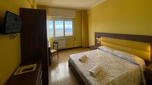A hotel room with a bed, a TV mounted on the wall, a desk, and a chair. - Hotel Robinia (Imperia)