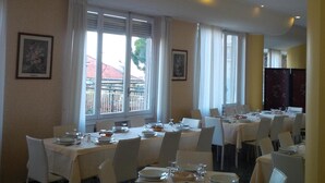A dining area with tables set for service, large windows with curtains, and framed artwork on the walls. - Hotel Robinia (Imperia)