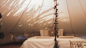 A tent with a bed, pillows, a woven basket, and a small table with candles. - Glamping La Ferme Tent II (Ingelmunster)