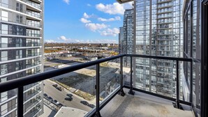 A high-rise building with a balcony overlooking a parking area and other buildings. - Newly Furnished 1BR Suite w Balcony & Free Parking (Mississauga)