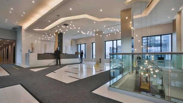 A spacious lobby with a reception desk, a glass railing, and a modern ceiling design. - Newly Furnished 1BR Suite w Balcony & Free Parking (Mississauga)