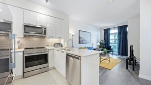 A modern kitchen with stainless steel appliances, a dishwasher, and a central island. - Newly Furnished 1BR Suite w Balcony & Free Parking (Mississauga)