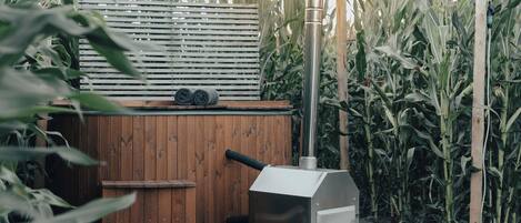 A hot tub with a wooden deck and a metal grill, surrounded by cornfield.