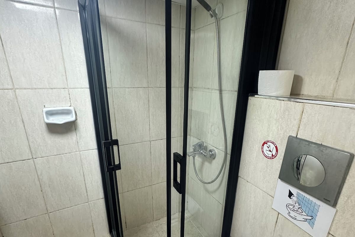 Un baño con ducha envuelta en vidrio, inodoro blanco y secador de manos montado en la pared.