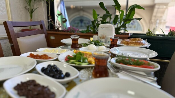A dining table with various dishes, including a croissant and a glass of tea, in a room with plants and a window. - Hotel Amore İstanbul (Istanbul)