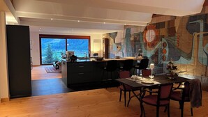 A modern kitchen with a large island, dining area with chairs, and a view of a snowy landscape through a glass door. - Graceland In the Black Forest (Fischerbach)