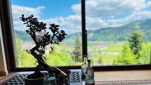 A bonsai tree, a bottle of water, and a bottle of schnapps on a tray by a window with a view of a green landscape. - Graceland In the Black Forest (Fischerbach)