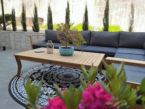 A patio area with a round patterned rug, a wooden table, a blue pot with a plant, a blue sofa, and a small table with a decorative item. - Graceland In the Black Forest (Fischerbach)