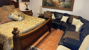 A bedroom with a bed, a black leather sofa, a nightstand with a lamp, and a framed painting on the wall. - Vista do Topo- Apartment (Povoacao)