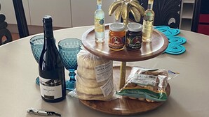 A round table with a bottle of wine, two glasses, a bread roll, a jar of jam, a bottle of liquor, and a bag of snacks. - Vista do Topo- Apartment (Povoacao)