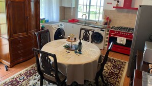 A kitchen with a dining area, including a table with chairs, a washing machine, a stove, and a cabinet. - Vista do Topo- Apartment (Povoacao)