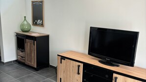 A modern living room with a glass coffee table, a television on a wooden cabinet, a green vase, and a framed picture on the wall. - Detached house with jacuzzi (La Sauvetat-du-Dropt)