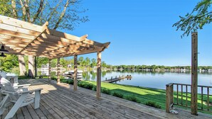 A wooden deck with a pergola, chairs, and a view of a lake. - Esther House - Beautiful, Newly Renovated Lakehouse on Paw Paw Lake (Watervliet)