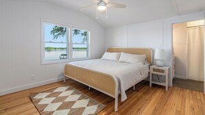 A bedroom with a bed, a nightstand, a ceiling fan, a window with a view, and a door with a curtain. - Esther House - Beautiful, Newly Renovated Lakehouse on Paw Paw Lake (Watervliet)