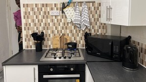 A kitchen with a gas stove, microwave, and a Samsung oven. There are two towels hanging on the wall and a knife block on the counter. - Remarkable 3-bed House in Liverpool (Liverpool)