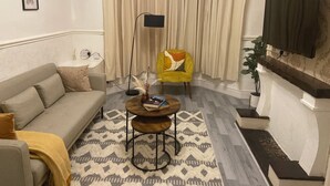 A living room with a sofa, a yellow armchair, a coffee table, a floor lamp, and a TV mounted on the wall. - Remarkable 3-bed House in Liverpool (Liverpool)