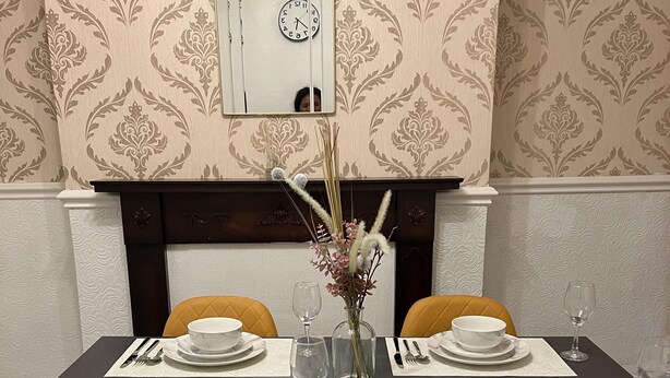 A dining room with a black table set for four, yellow chairs, a vase with flowers, and a clock on the wall. - Remarkable 3-bed House in Liverpool (Liverpool)